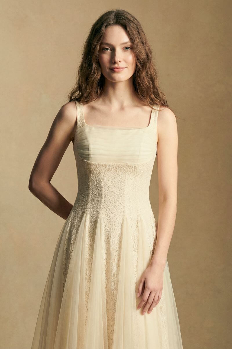 Model wearing an ivory lace midi dress featuring a structured lace bodice, sheer tulle overlay, and slim shoulder straps, photographed in a softly lit studio setting.