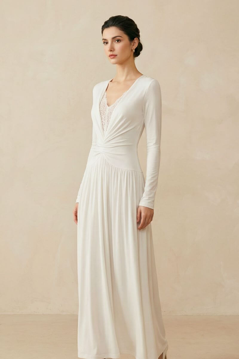 A model wears an ivory long sleeve maxi dress with a softly ruched waist and lace V-neck detail, styled with neutral heels against a warm beige studio backdrop.