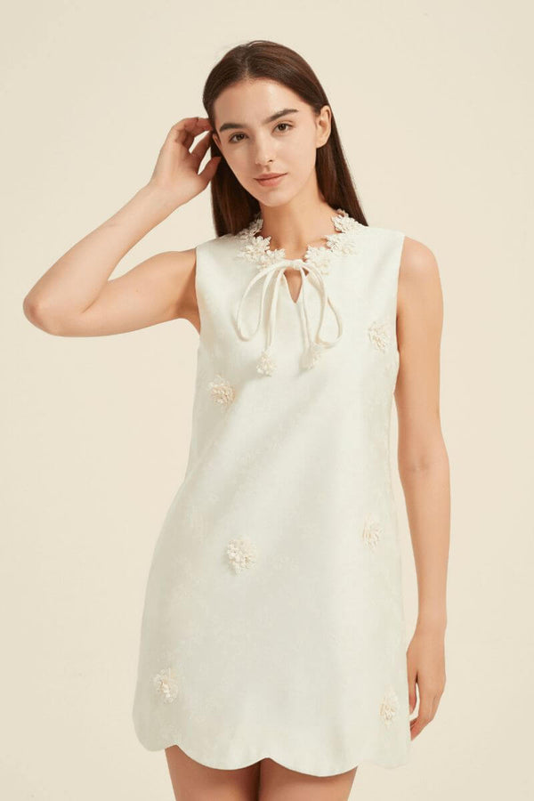 Closeup showing tie-neck with floral trims and textured floral appliqué on an ivory mini dress.