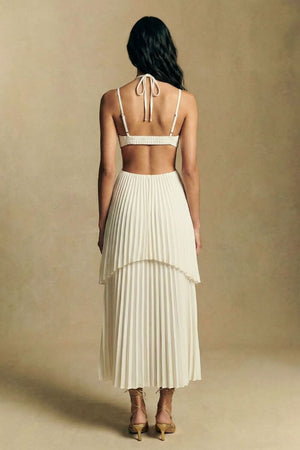 Back view of an ivory pleated midi dress revealing an open back with tie straps and a layered pleated skirt, styled with lace-up heels.