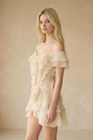 A side view of a model wearing an ivory off-shoulder ruffled mini dress, highlighting the layered chiffon texture and fluid drape along the skirt.