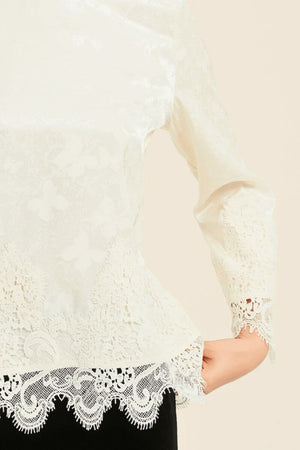 Close-up of ivory satin blouse featuring delicate butterfly jacquard and scalloped lace trim along hem and cuffs — a romantic feminine top by Sioéne.
