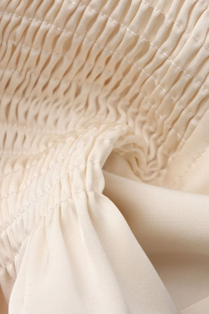 A close-up image of ivory textured satin fabric with delicate smocking details, showing the soft, lightweight drape and gathered construction.