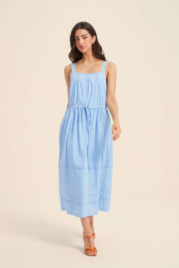 Woman wearing a light blue pintuck midi dress with lace shoulder straps and a tie waist, styled with tan heels for a fresh and effortless daytime look.