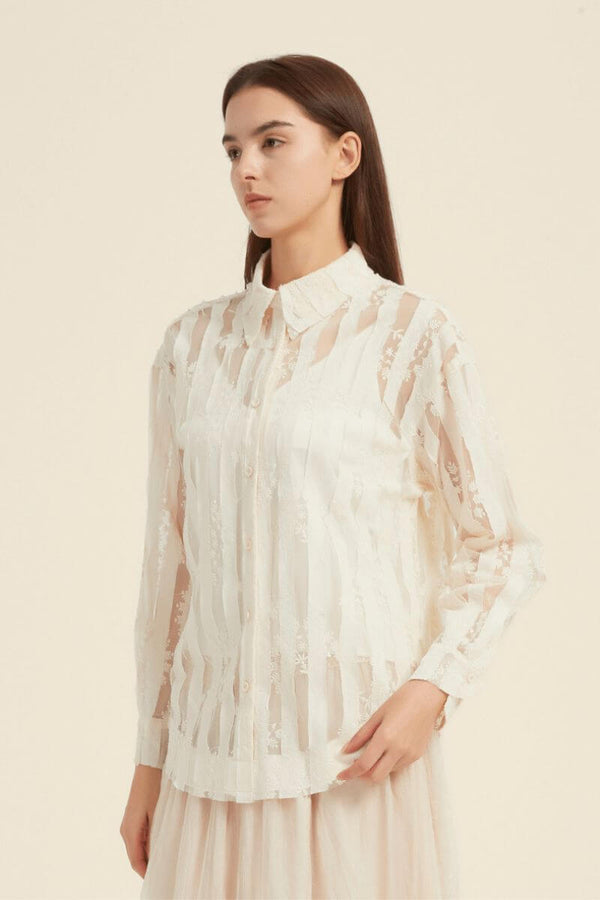 Woman wearing a cream long-sleeve sheer lace blouse with button-down design and floral embroidery, styled with a cream midi skirt indoors.
