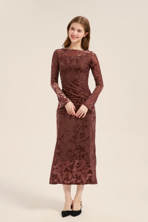 Model wearing a mocha-colored burnout velvet midi dress with long sleeves, boat neckline, and subtle floral texture, paired with black heels.