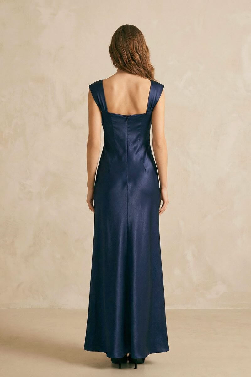 Back view of a navy satin maxi dress showing wide shoulder straps, a clean straight back neckline, and a fluid full-length skirt.