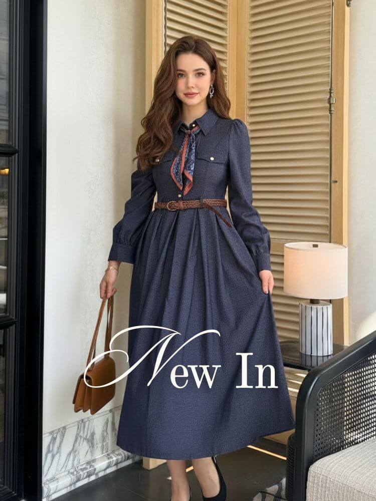 Woman in a navy long-sleeve midi dress with a belted waist and printed scarf tie, standing in a bright modern terrace setting — showcasing the latest Sioéne arrivals.