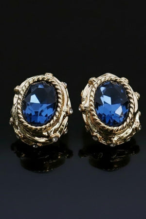 A pair of vintage-inspired gold stud earrings featuring deep navy faceted stones set in a textured, rope-style gold frame against a black background.