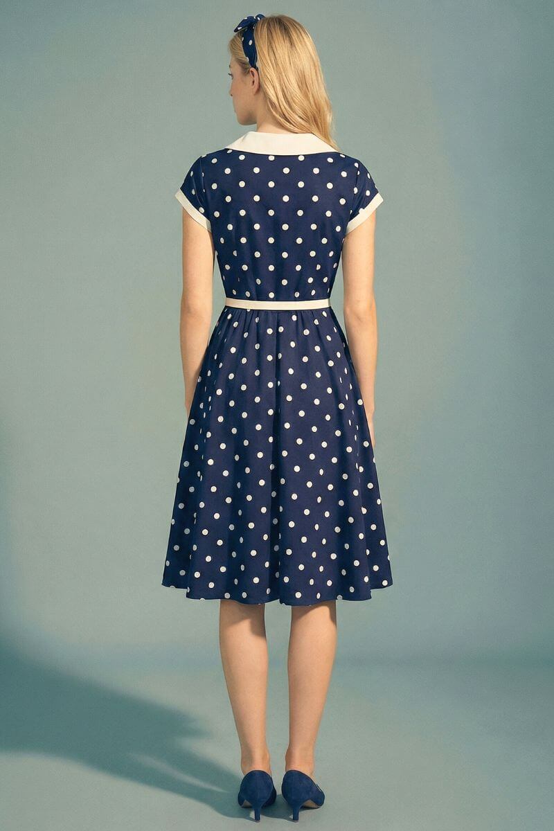 Back view of a navy polka dot midi dress with a contrast ivory collar and defined waist, highlighting the clean back construction and softly flared skirt.