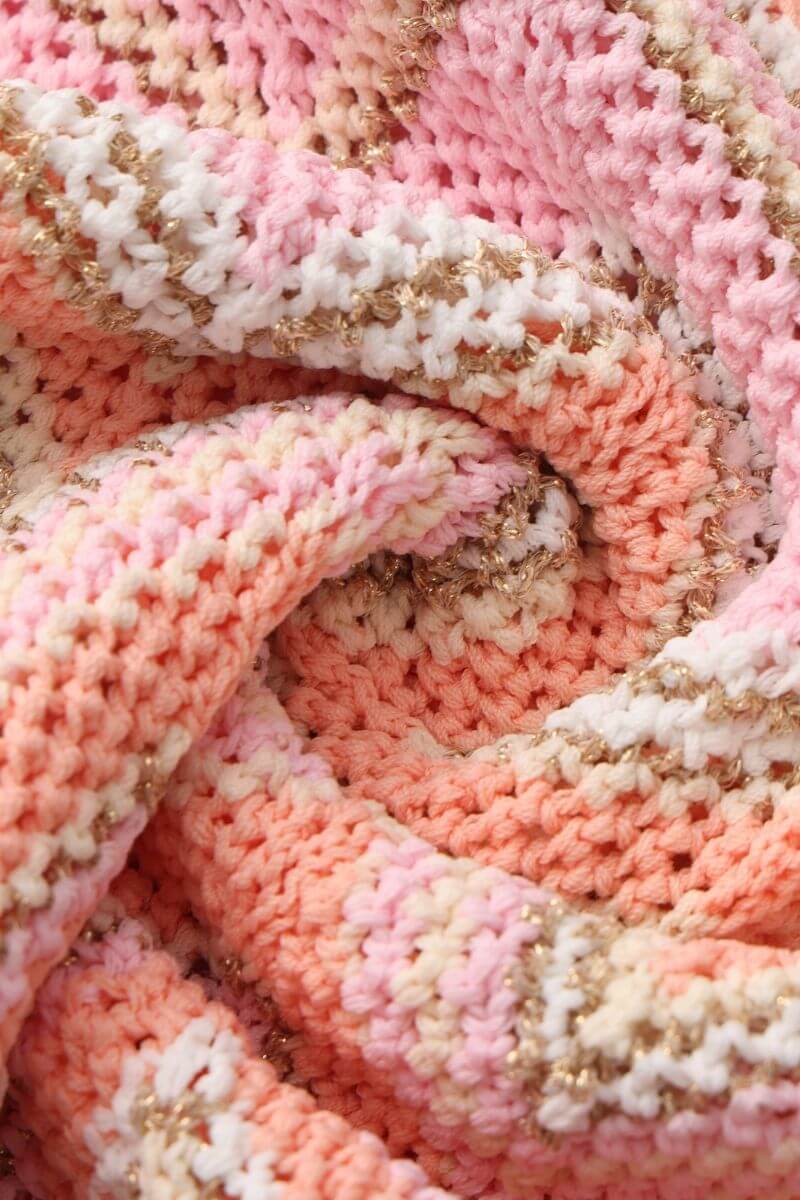 Close-up of the peach and pink chevron knit fabric with gold-thread accents, showing the textured crochet-style stitching and colorful woven pattern.