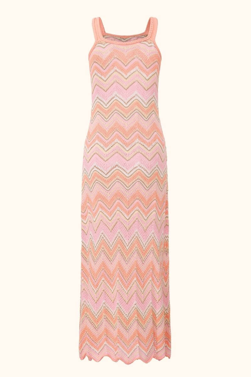 The back view of a peach-pink chevron knit maxi dress showing the same textured zigzag knit pattern and long straight hem with a scalloped edge.