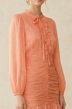 Detailed close-up of the peach midi dress fabric showcasing fine sheerness, soft ruching through the waist, and delicate ruffle trims.