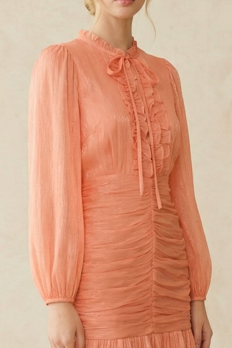 Detailed close-up of the peach midi dress fabric showcasing fine sheerness, soft ruching through the waist, and delicate ruffle trims.