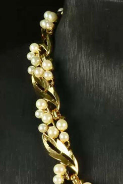Detailed view of a gold leaf necklace with clustered pearl accents, emphasizing the textured metal and organic arrangement.
