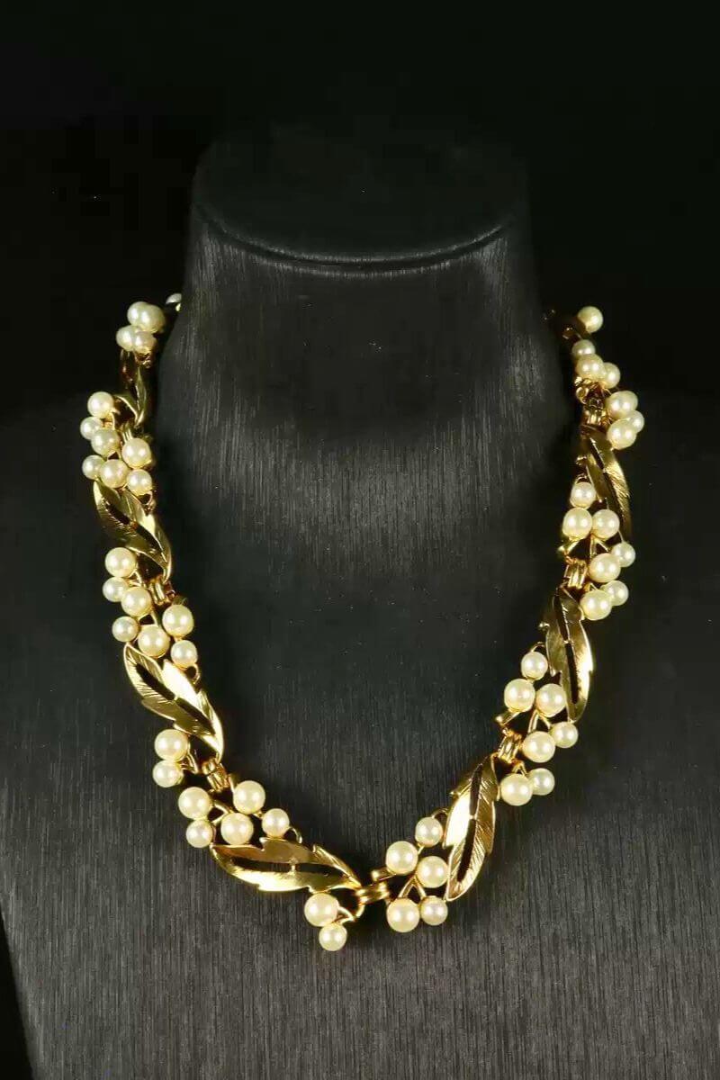 Front view of a vintage-style gold necklace featuring layered leaf links and evenly spaced round pearls displayed on a black bust.