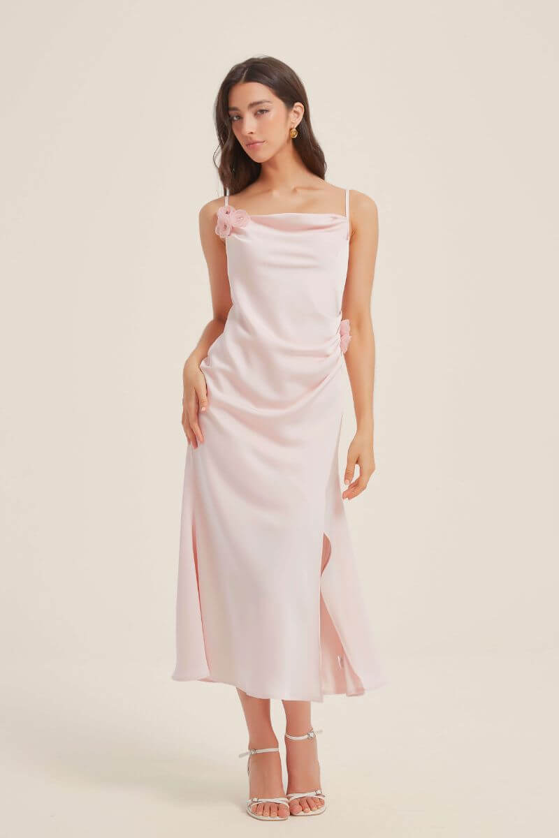 Close-up of a pink satin midi dress highlighting the draped cowl neckline and delicate floral appliqué at the shoulder and waist.