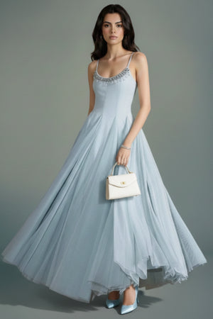 Model styling a powder blue tulle maxi dress with subtle beaded neckline, paired with light blue heels and a structured ivory handbag for an elegant evening look.