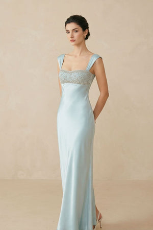 Side view of a model in a powder blue satin maxi dress showing the clean silhouette, wide shoulder straps, and subtle sheen of the satin fabric.