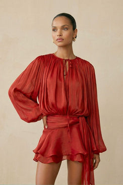 The model stands in a red chiffon mini dress with voluminous sleeves, a wrapped waist tie, and a gently flared ruffle skirt, creating a romantic and fluid silhouette.