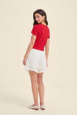 Back view of a woman wearing a red short-sleeve crop tee paired with white embroidered shorts, showing the simple clean silhouette of the Sioéne fruit print top.