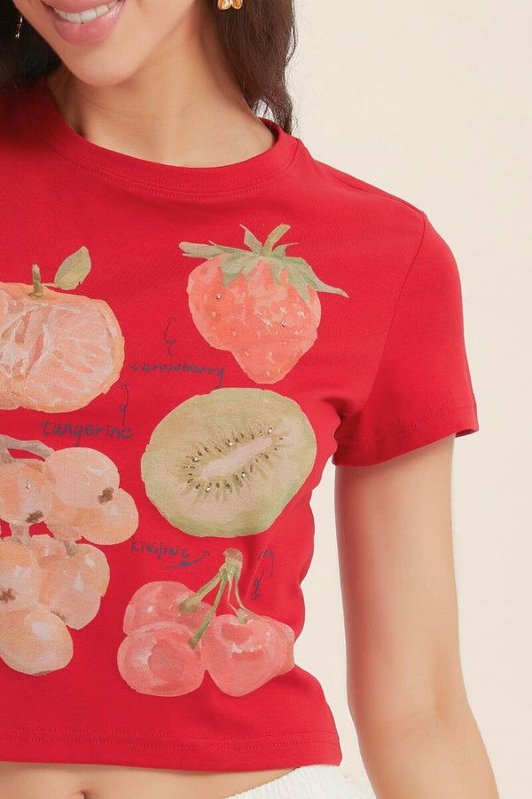 Close-up of a red Sioéne T-shirt featuring painted fruits including strawberry, kiwi, tangerine, and cherry with subtle rhinestone accents for a fresh summer touch.