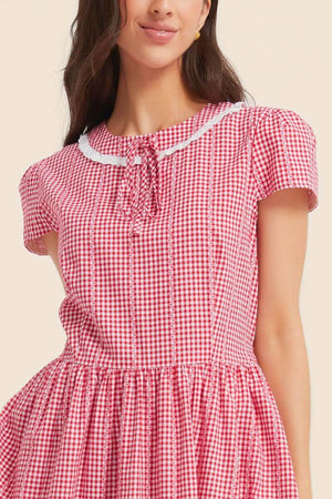 Close-up of a red and white gingham midi dress featuring a lace-trim Peter Pan collar, tie-neck detail, and short puff sleeves.
