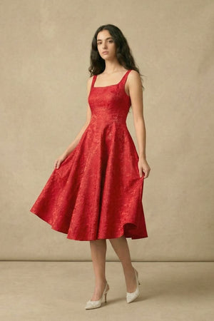 A woman gently lifting the hem of her red jacquard midi dress to show the flowy A-line silhouette, standing in a studio.