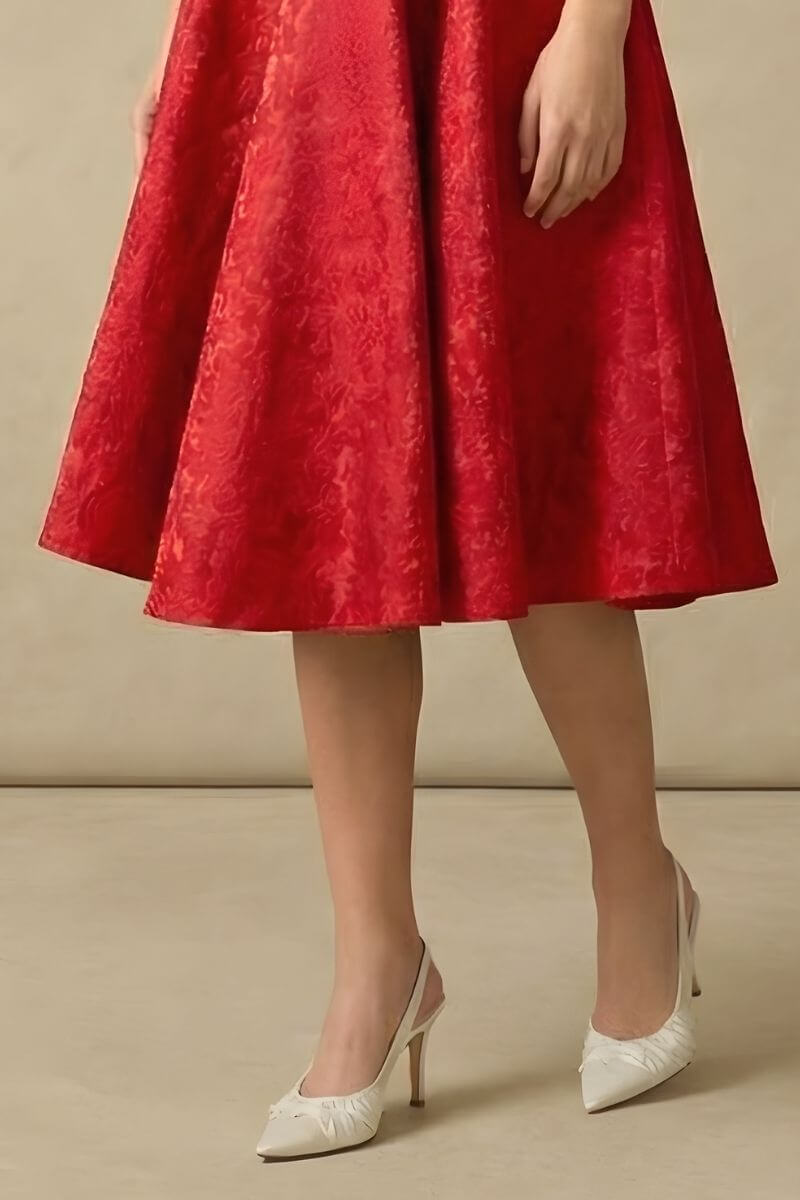 A woman wearing a red jacquard fit-and-flare midi dress with a square neckline, photographed at a three-quarter angle in a neutral studio.