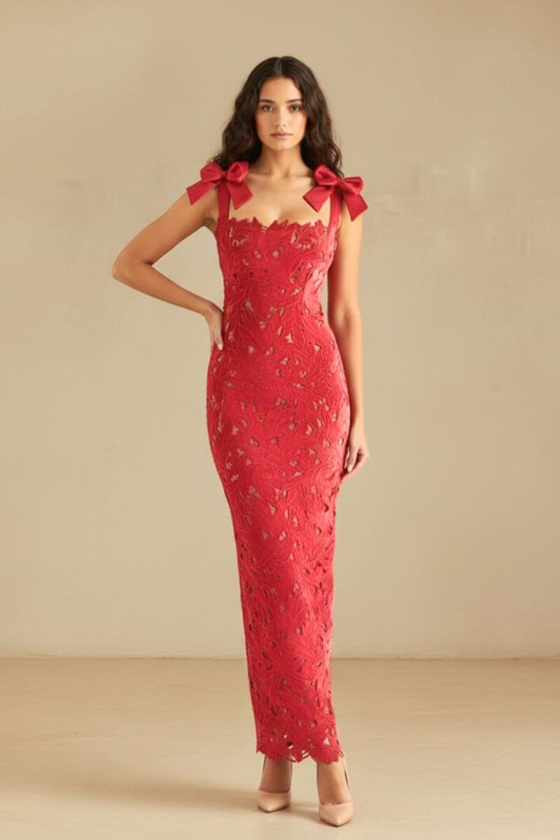 Full-length view of a woman wearing a red lace bow-shoulder maxi dress with a fitted silhouette and nude heels on a neutral background.