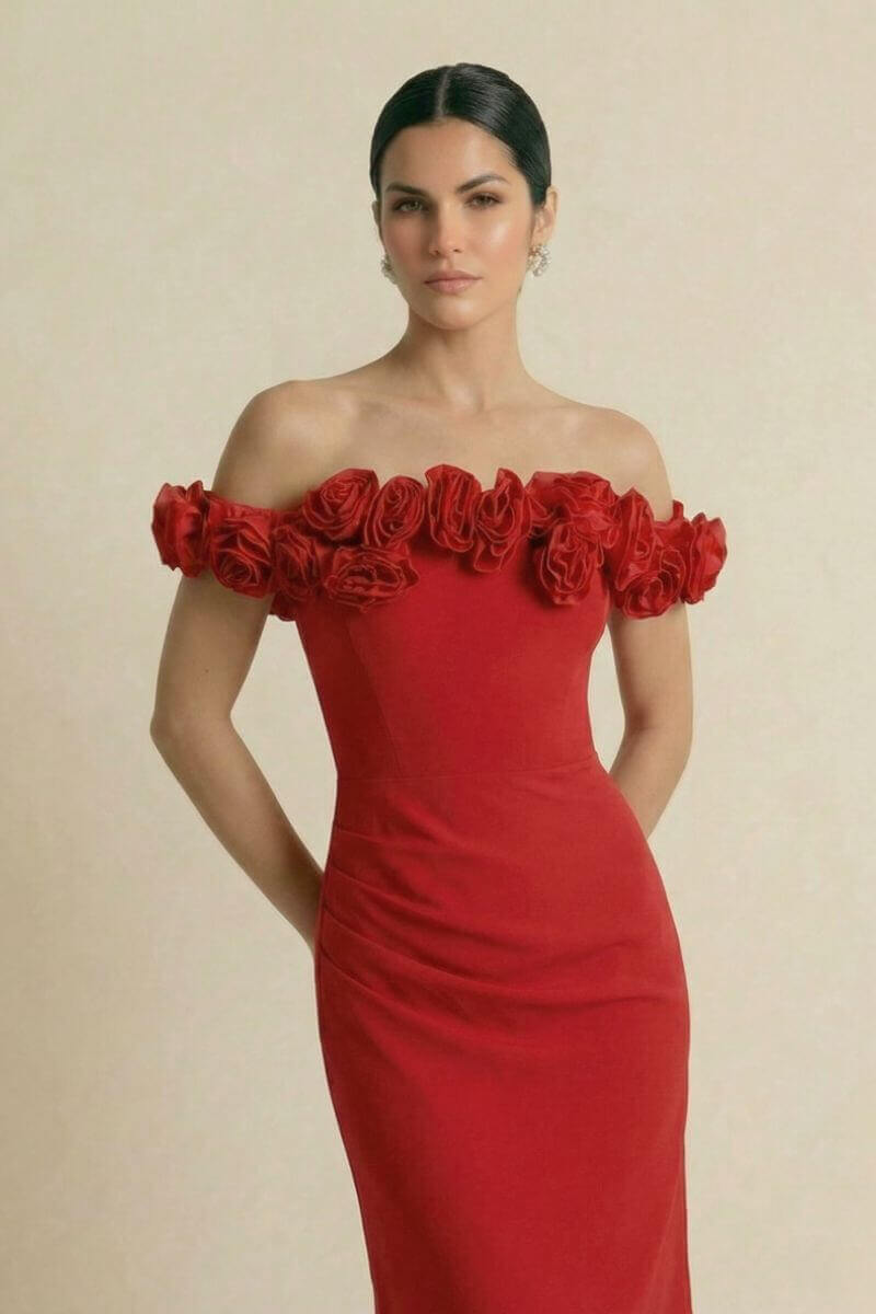 A model wearing an off-shoulder red gown adorned with sculpted rosette trim across the neckline, posing against a neutral studio background in an elegant, refined look.