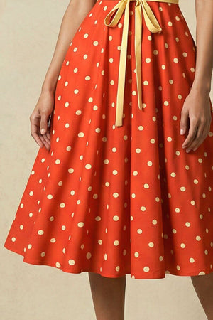 Detailed view of the red polka dot midi dress skirt showing soft pleats, lightweight fabric movement, and evenly spaced ivory polka dots.