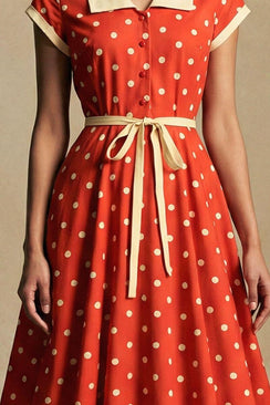 Close-up of the red polka dot midi dress highlighting the cinched waist, cream ribbon tie belt, and fluid skirt drape with a vintage-inspired silhouette.