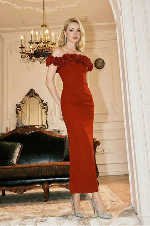 A model in a luxurious red off-shoulder rosette gown stands in a vintage-inspired interior with chandeliers and ornate furnishings, showcasing the elegant long silhouette and sculpted neckline.