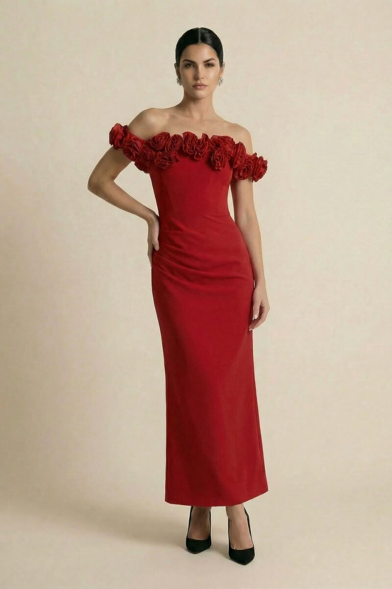 A model poses in a full-length red off-shoulder gown featuring a dramatic rosette neckline and a smooth, body-skimming silhouette against a soft beige studio backdrop.