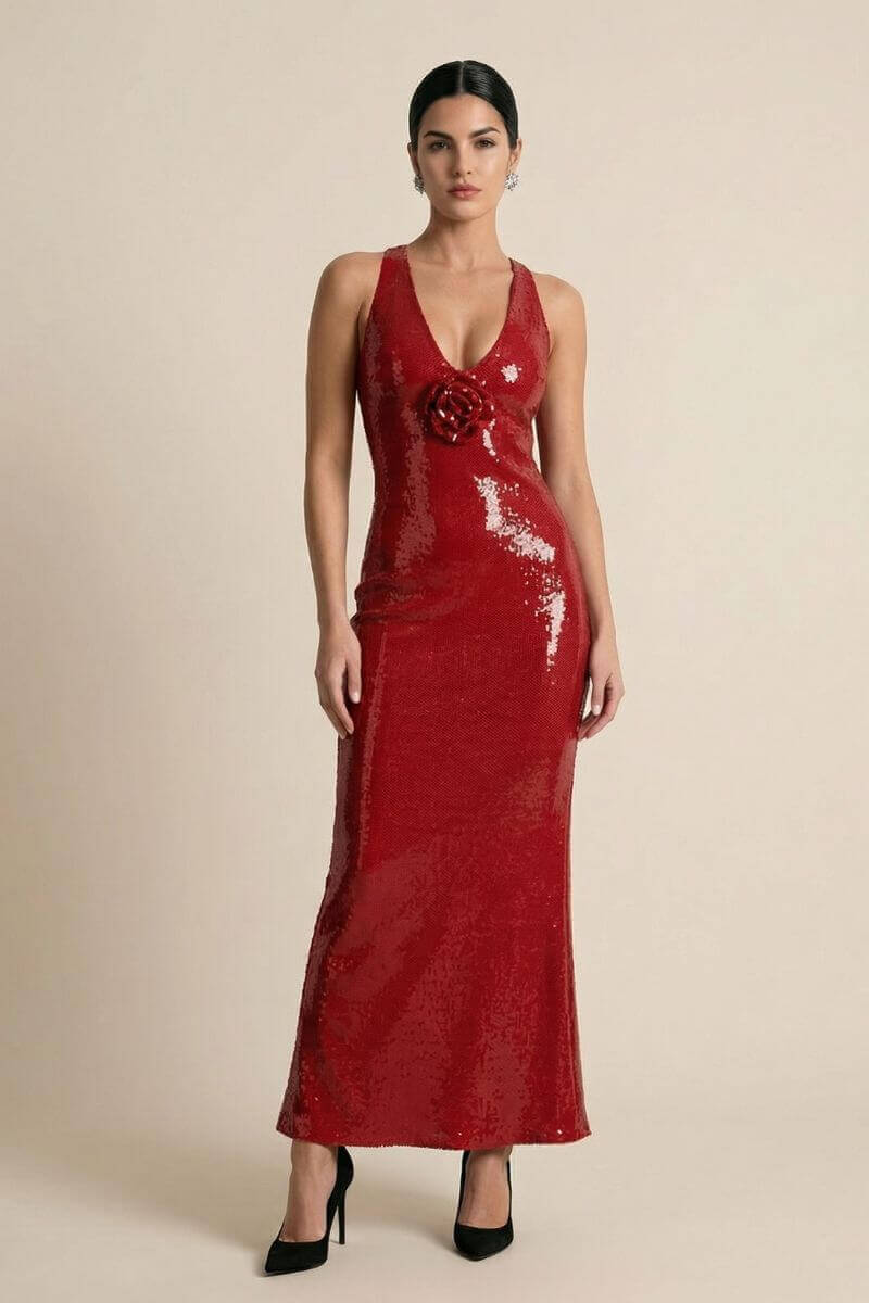 Model wearing a red sequin halter-neck maxi dress with a deep V-neckline and a sculpted rose appliqué at the bust, styled with black heels against a neutral studio background.