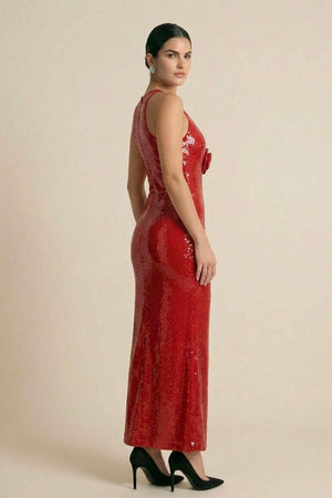 Side view of a model in a red sequin form-fitting halter maxi dress featuring a smooth, reflective finish and black pointed heels, photographed in a minimal beige studio.