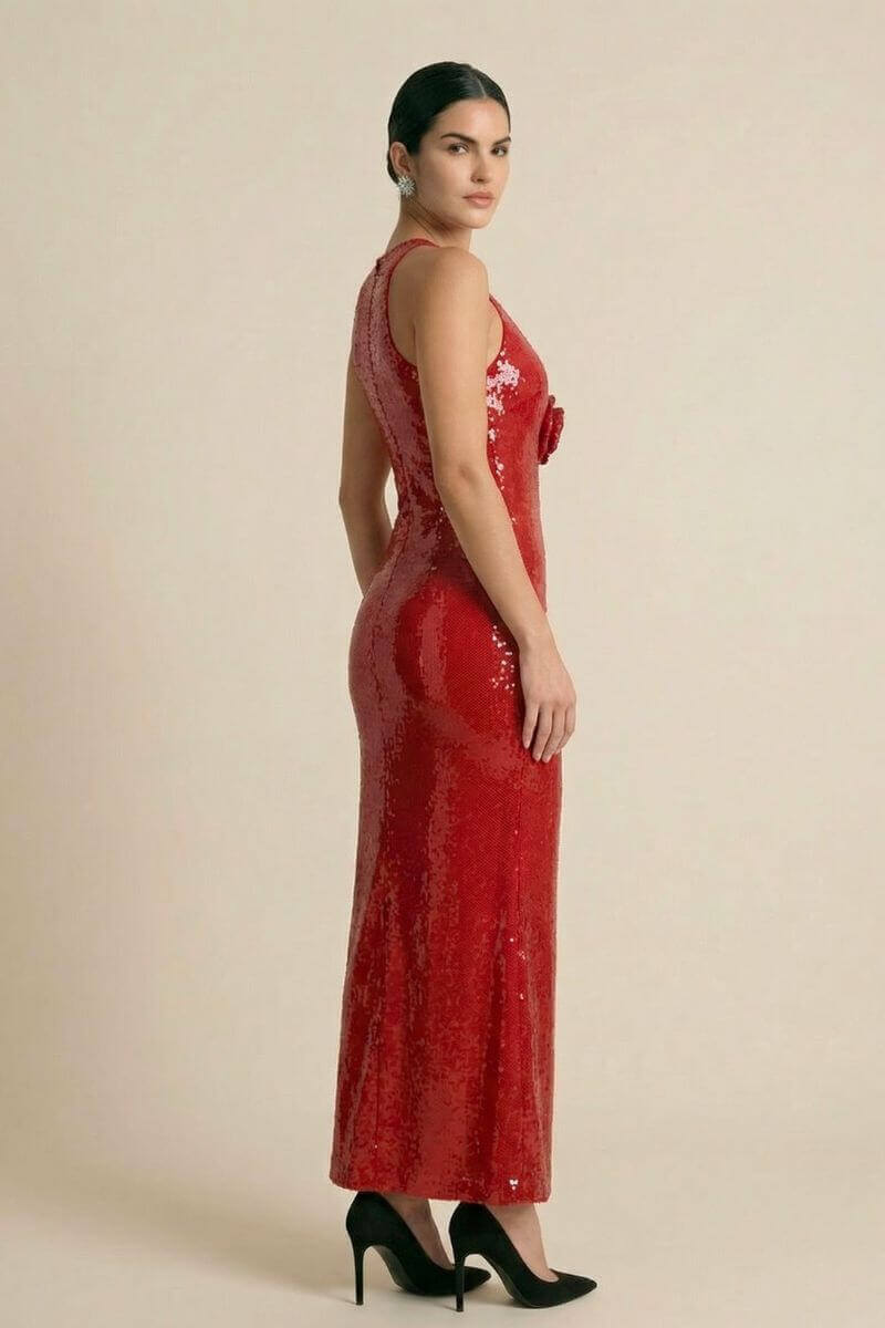 Side view of a model in a red sequin form-fitting halter maxi dress featuring a smooth, reflective finish and black pointed heels, photographed in a minimal beige studio.