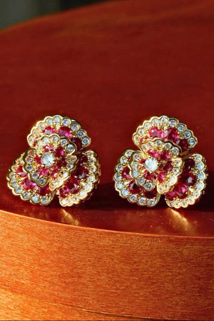 A pair of ruby and clear crystal flower stud earrings in gold setting, photographed symmetrically against a black background.
