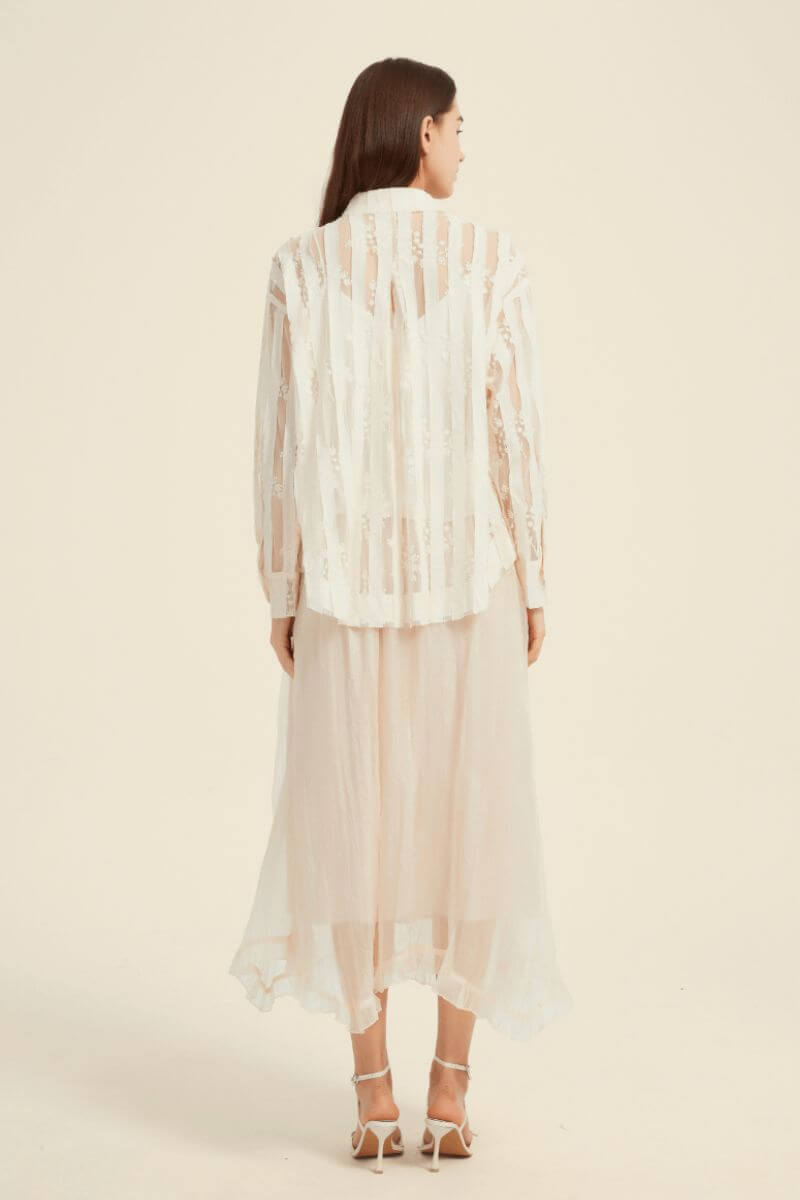 Back view of a model wearing a sheer cream lace button-up blouse paired with a soft layered tulle midi skirt.