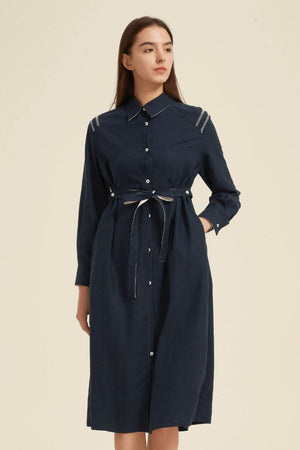 Side angle of a navy collared midi shirt dress with front buttons and waist tie, styled with brown ankle boots for a polished modern look.