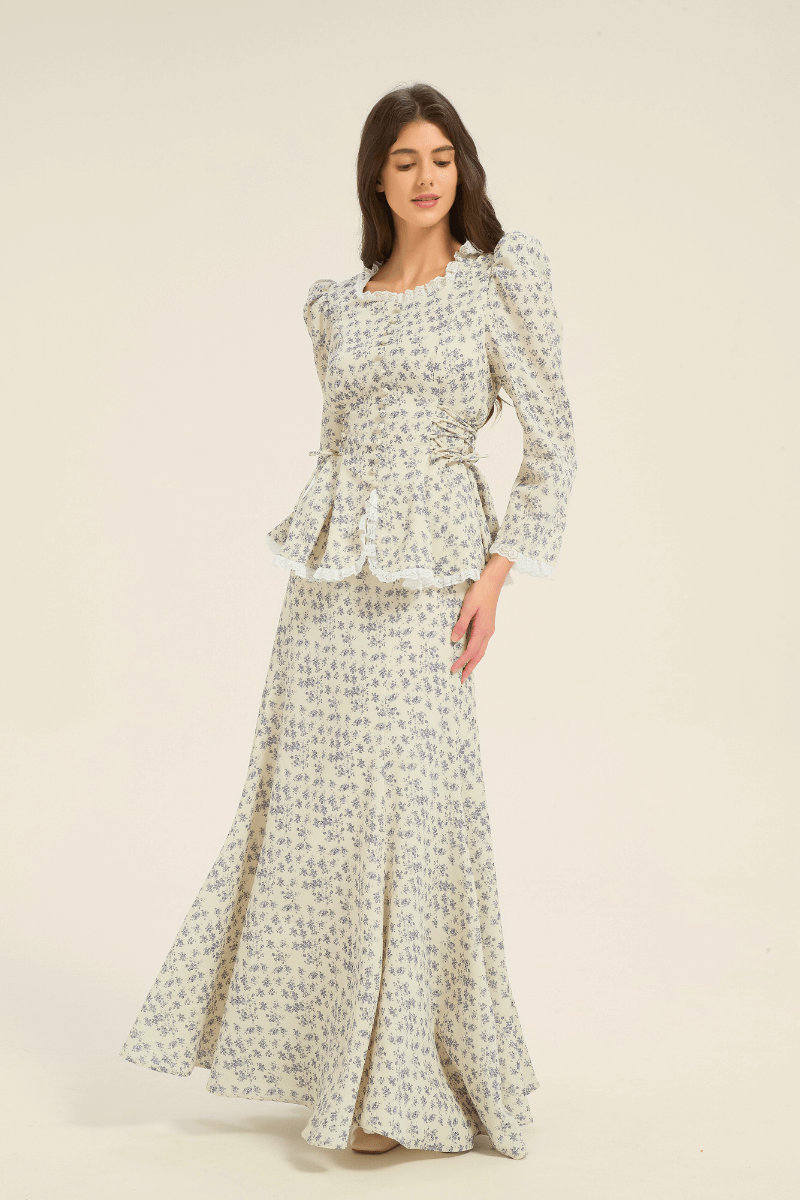 Model in cream and blue floral two-piece set with peplum top and flowing maxi skirt, shown from the side.