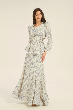Model in cream and blue floral two-piece set with peplum top and flowing maxi skirt, shown from the side.