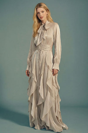 A front view of a silver satin maxi dress featuring a bow-tie neckline, long sleeves, layered ruffle skirt, and softly structured waist for an elegant evening silhouette.