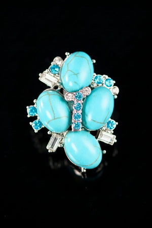 A close-up front view of a turquoise cluster stud earring featuring oval turquoise stones arranged in a floral shape with clear crystal accents on a black background.

