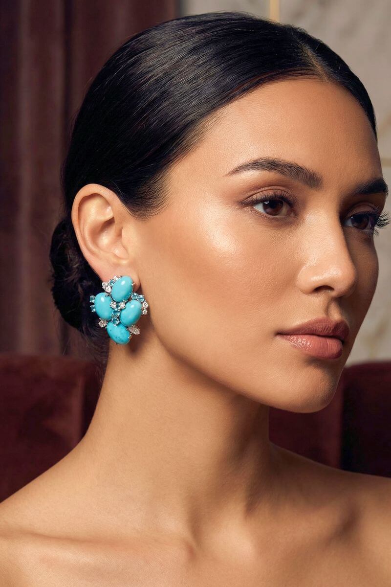 A model wears the turquoise cluster stud earrings styled with slicked-back hair, highlighting the bold floral silhouette and vivid turquoise tones against warm skin.