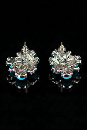 The back view of turquoise cluster stud earrings showing silver-tone posts and secure butterfly backs, photographed on a glossy black surface.
