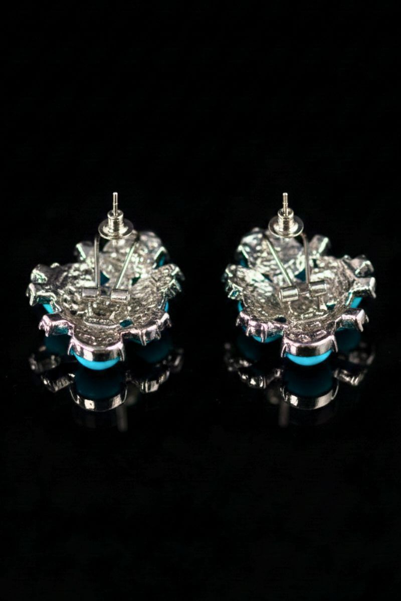 The back view of turquoise cluster stud earrings showing silver-tone posts and secure butterfly backs, photographed on a glossy black surface.