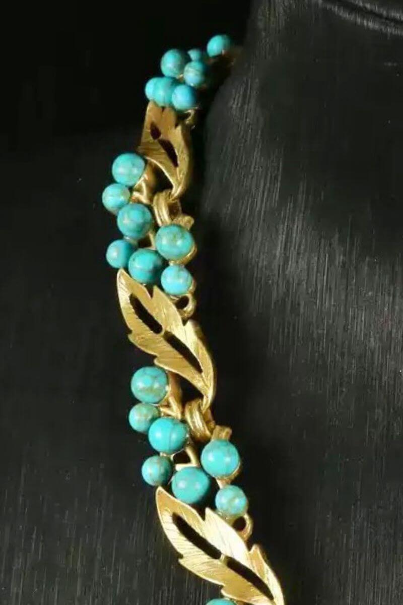 Close-up of a vintage-inspired gold bracelet featuring sculpted leaf motifs and clustered turquoise beads against a black background.