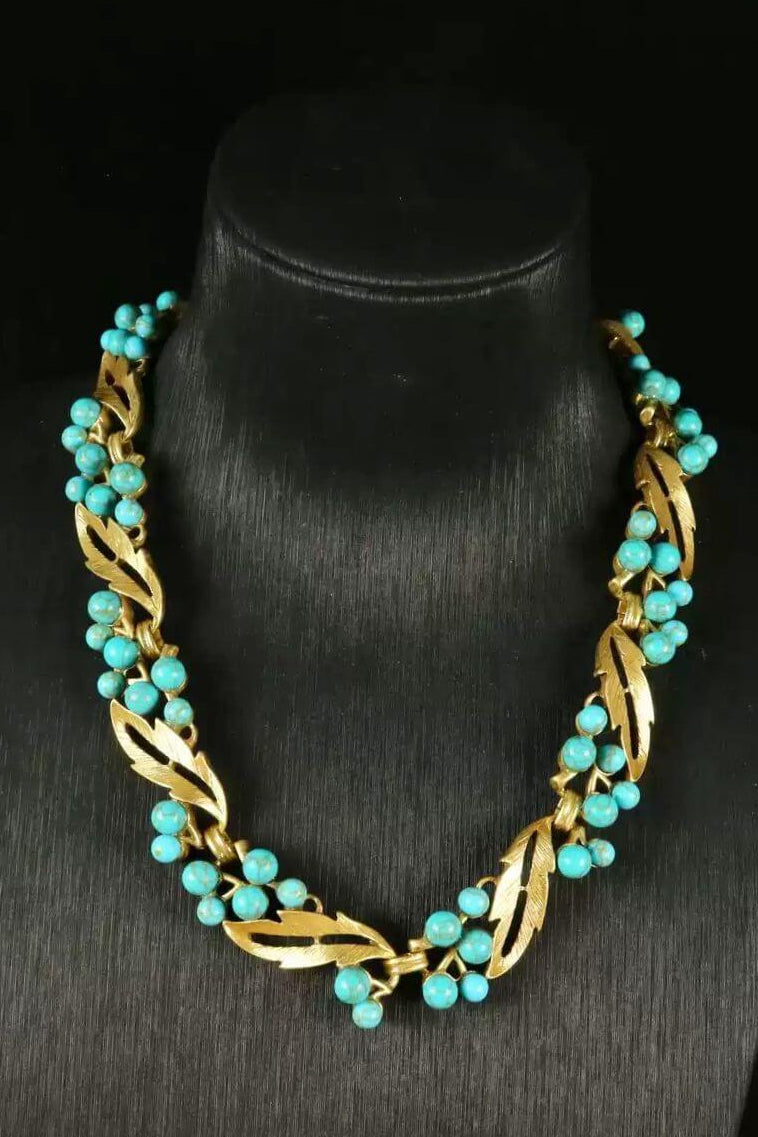 Front view of a gold leaf necklace adorned with turquoise bead clusters, displayed on a black bust for contrast and clarity.